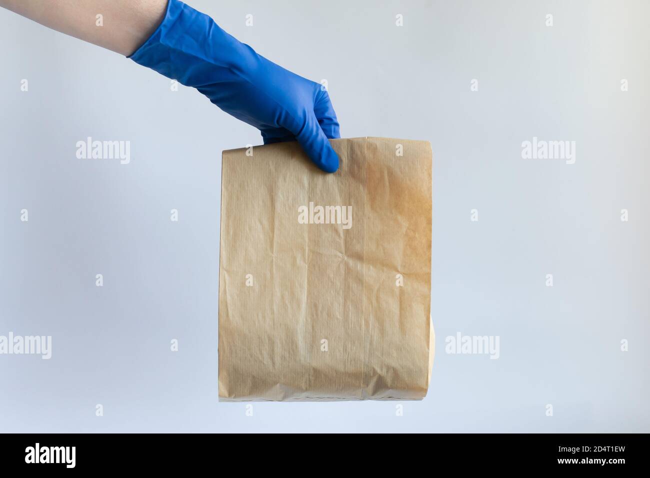 La mano maschile in un guanto protettivo tiene un sacchetto di carta con il cibo. Consegna di cibo, donazione di cibo. Quarantena di coronavirus. Concetto di servizio di consegna. Foto Stock