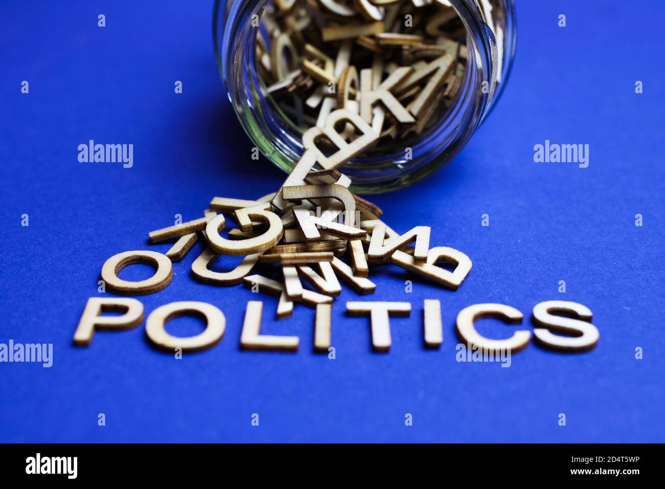 Primo piano di boccato sopra vaso di vetro con caotico sparso lettere alfabetiche su sfondo blu che formano la parola politica Foto Stock