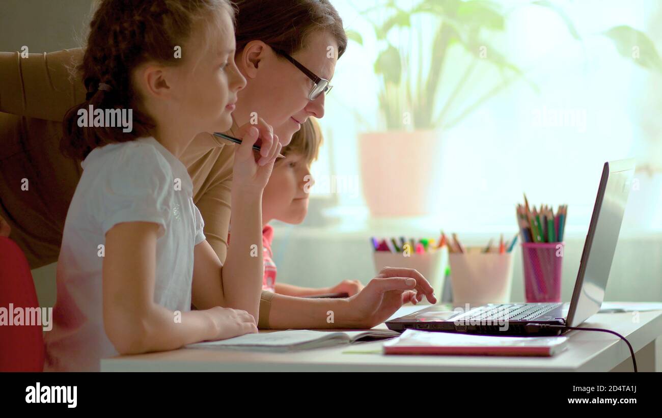 I bambini carini usano il laptop per l'istruzione, lo studio in linea, lo studio domestico, il ragazzo e la ragazza hanno compiti a distanza imparando. Concetto di stile di vita per la scuola domestica. Madre aiuta figlia e figlio. Foto Stock