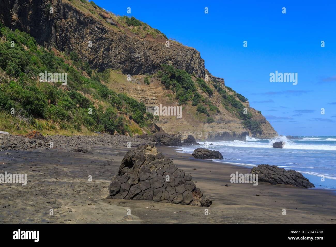 Una spiaggia di sabbia nera a Maukatia Bay sulla costa occidentale della regione di Auckland, Nuova Zelanda. Grumi di lava "a cuscino" si trovano sulla riva Foto Stock