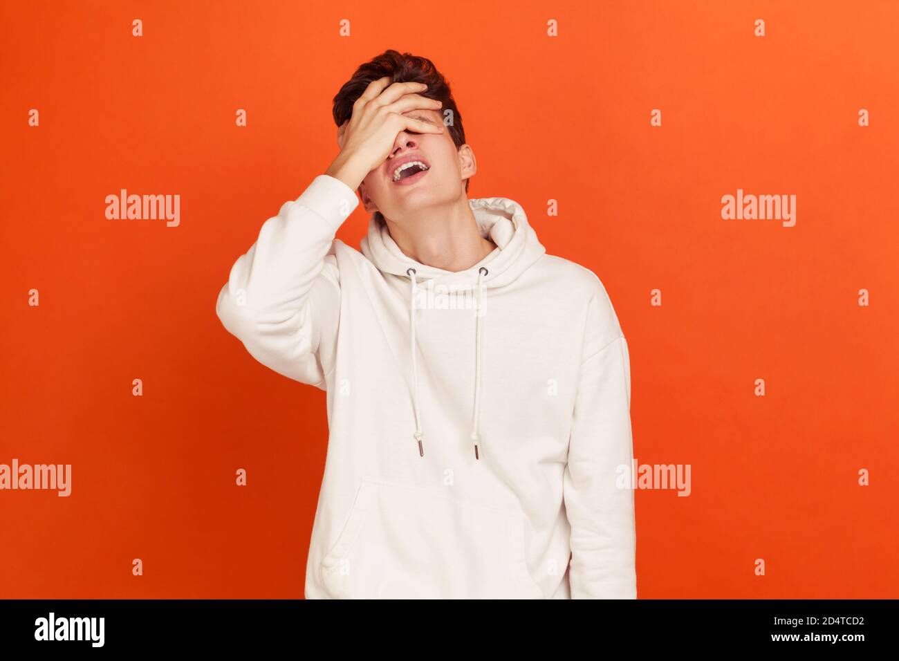 Depresso giovane uomo in stile casual bianco felpa con cappuccio chiusura occhi con braccio, facendo facepalm gesto, perdente, dimenticare qualcosa di importante. studi interni Foto Stock