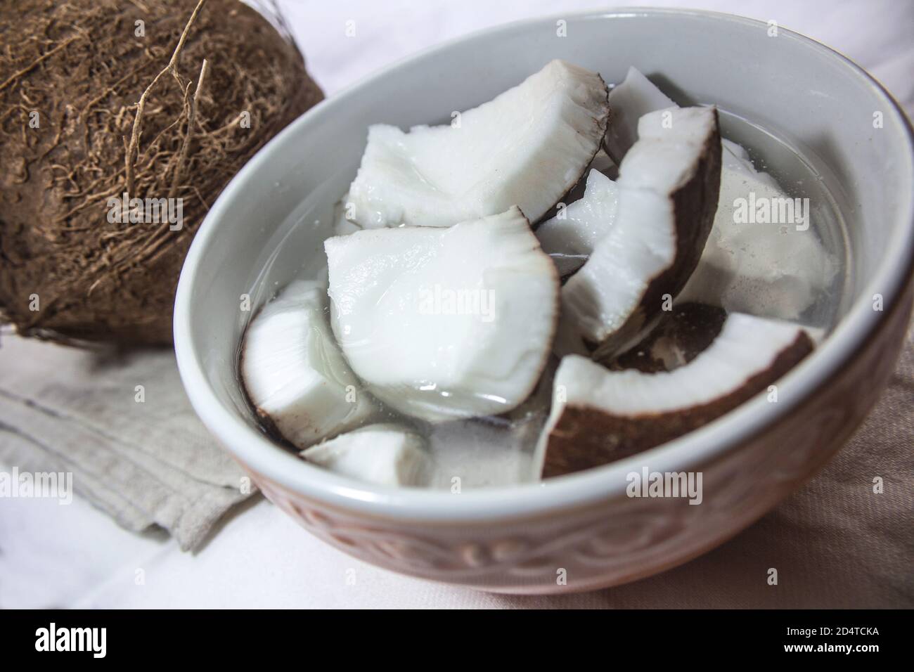 Pezzi di cocco fresco immersi in acqua in una ciotola, sullo sfondo un intero cocco Foto Stock