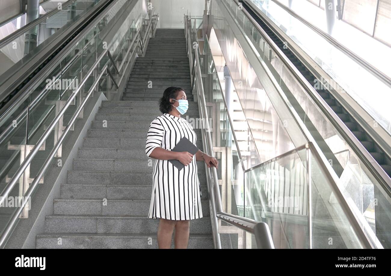 Uomo d'affari che indossa la maschera facciale con la mano sulla ringhiera, in piedi su scala che guarda fuori Foto Stock