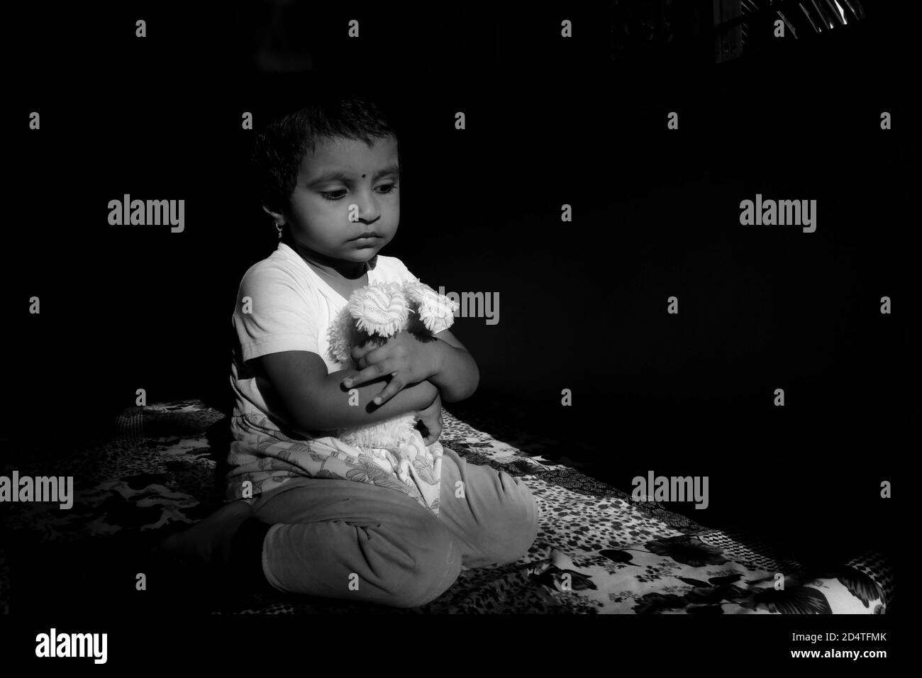 Bambina indiana che tiene la bambola in posizione seduta a forma di W nella foto monocromatica a luce bassa, Kalaburagi, Karnataka/India-Ottobre 09 2020 Foto Stock