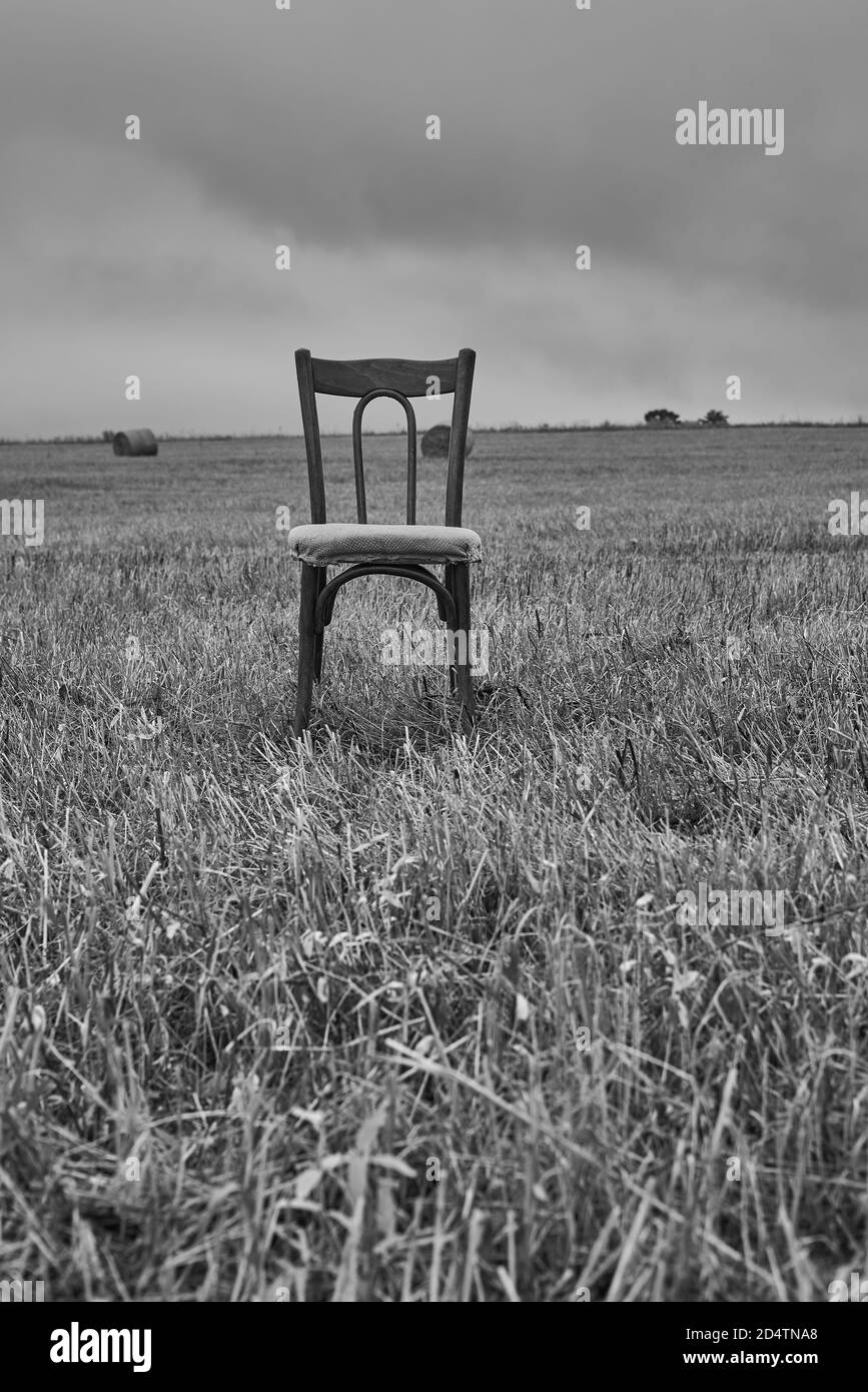 Una vecchia sedia si trova in un campo di falda contro un cielo nuvoloso. Foto Stock