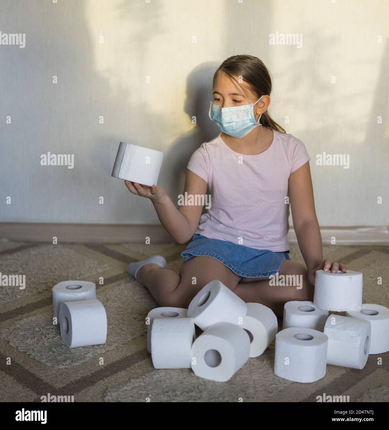 Una ragazza in maschera medica gioco con rotoli di carta igienica seduta  sul pavimento. Il hype circa la domanda di carta igienica durante la  pandemia globale del coronavirus Foto stock - Alamy
