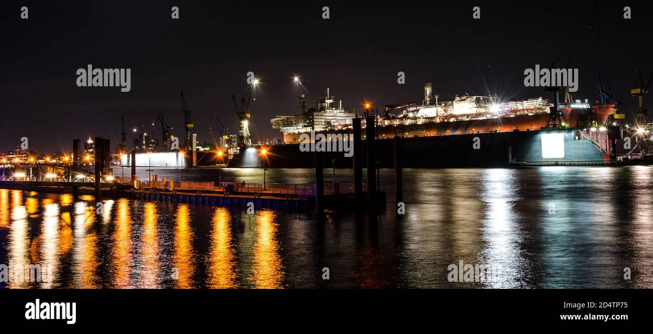 Panoramica widescreen ripresa notturna di una grande nave container in riparazione nel molo sul fiume Elba ad Amburgo, Germania Foto Stock