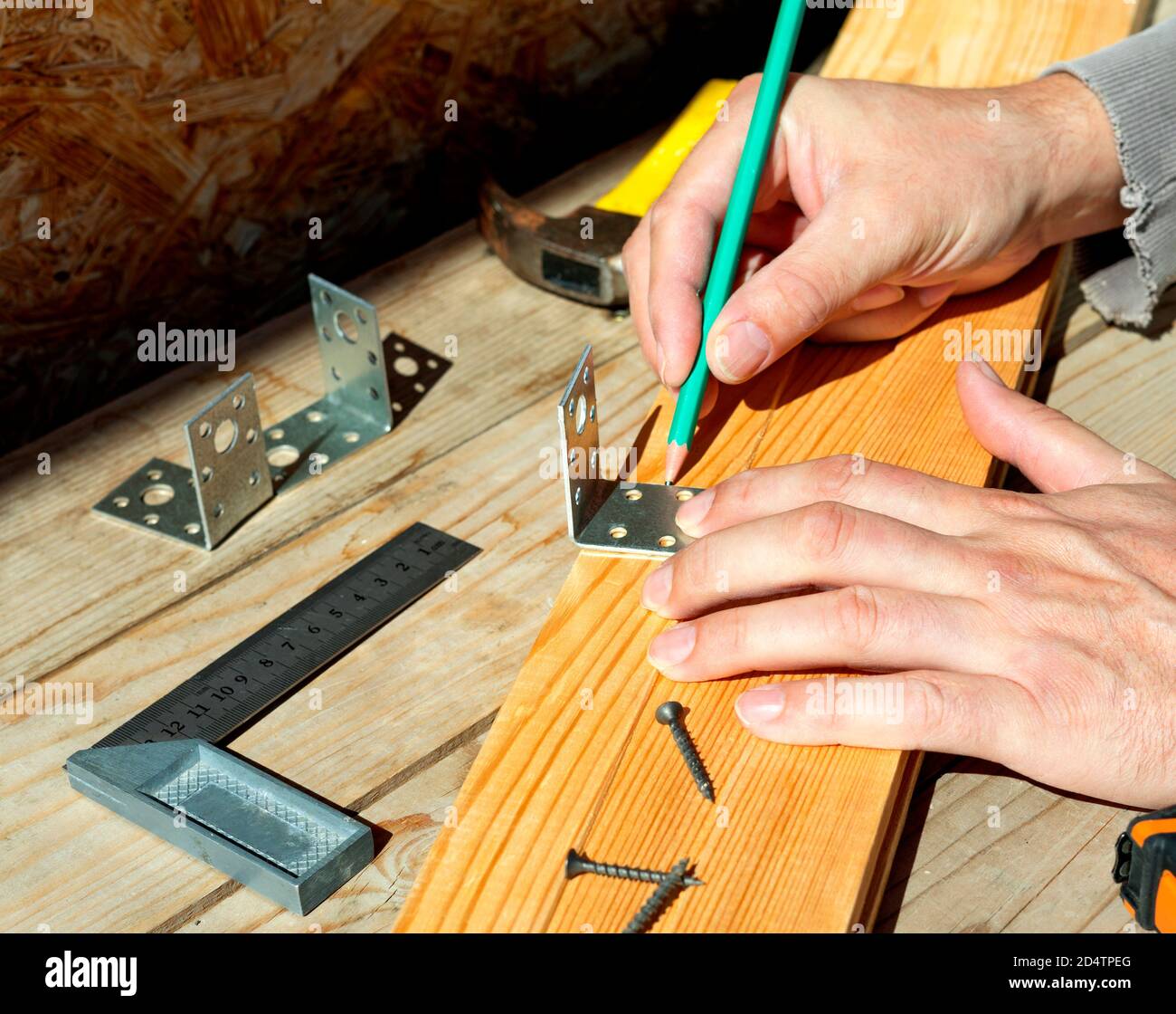 Il falegname cerca su un angolo di mobili usando una matita. Apporta un segno prima di avvitare l'angolo alla tavola di legno. Foto Stock