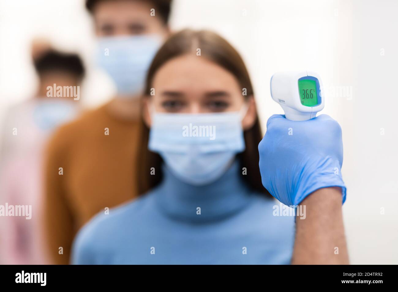 Lavoratore medico che fa lo screening della temperatura per Lady in Queue Indoor Foto Stock