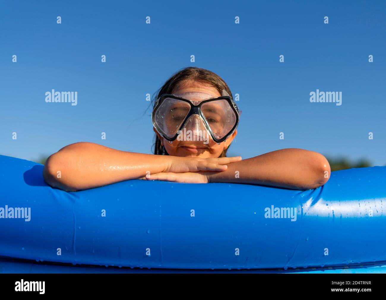 Una ragazza carina in una maschera subacquea sta riposando sul bordo di una piscina gonfiabile. Foto Stock