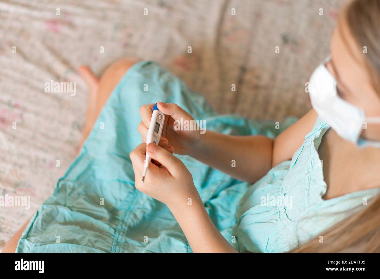 Una ragazza in una maschera medica contiene un termometro elettronico. Rimani a casa. Rimani al sicuro. Foto Stock