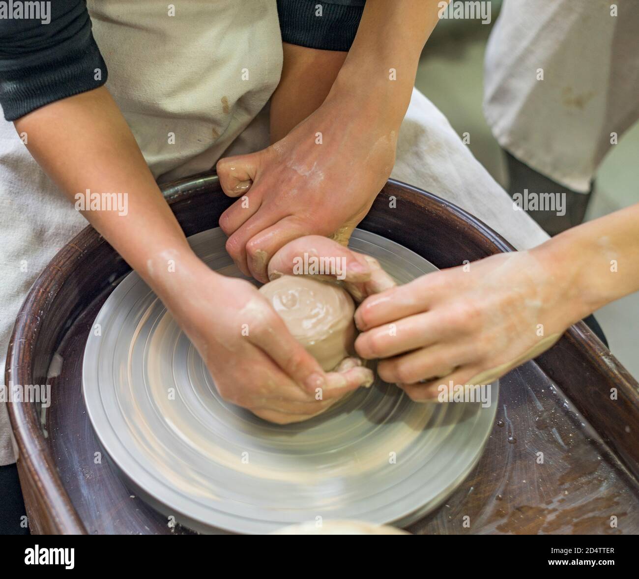 Un vasaio mani che guidano un bambino mani per aiutarlo a lavorare con la ruota di ceramica e l'argilla. Primo piano della foto dell'officina. Apprendimento in corso. Foto Stock