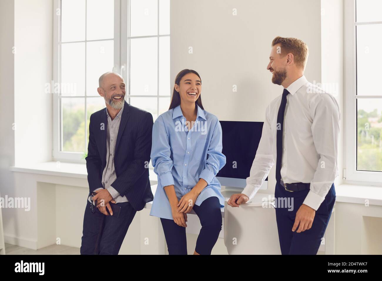 Giovani uomini d'affari sorridenti che si guardano l'un l'altro in ufficio durante l'avvio o la discussione sul progetto Foto Stock