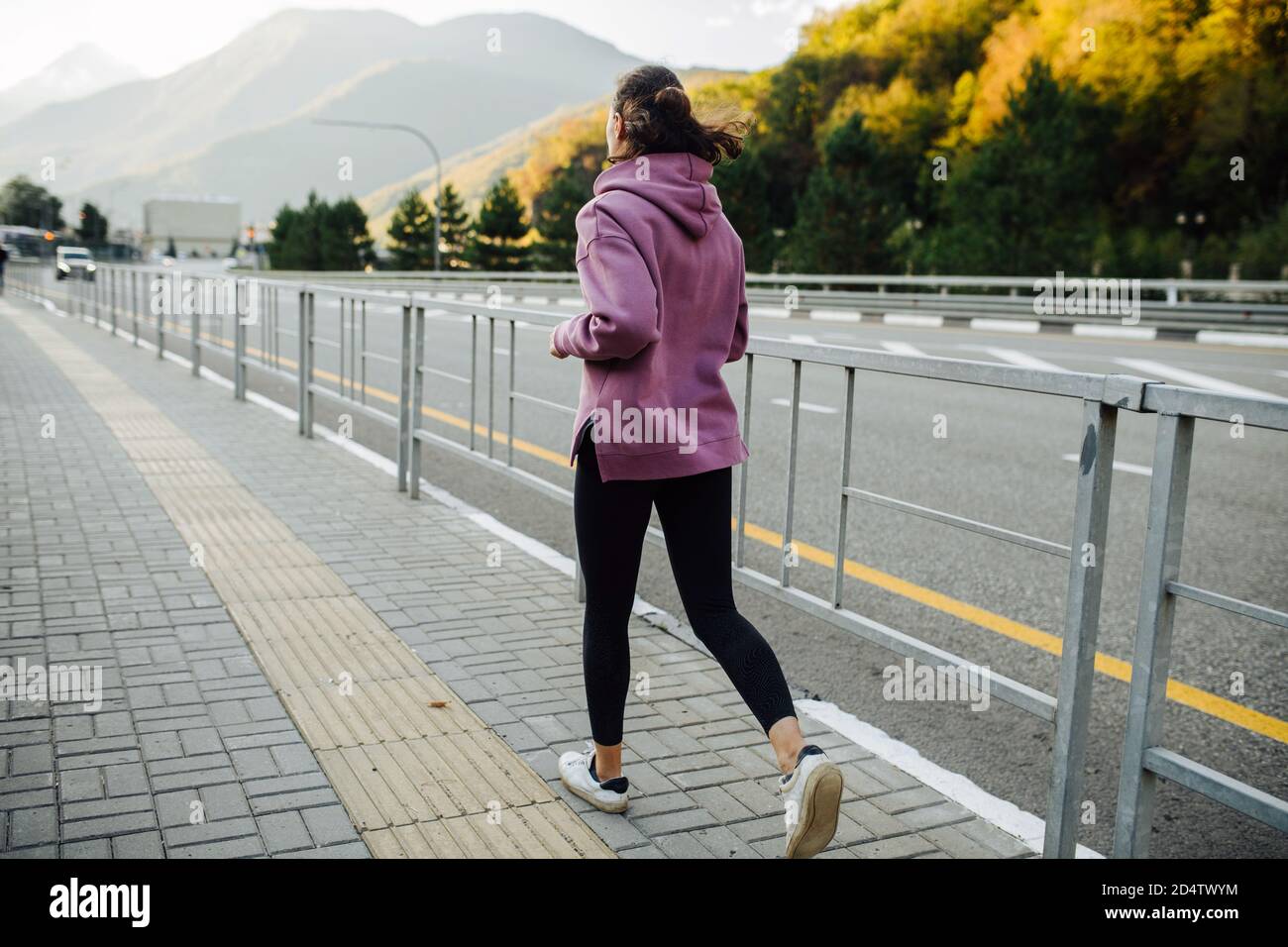 Donna che corre su un marciapiede con barriera in acciaio lungo autostrada di montagna Foto Stock