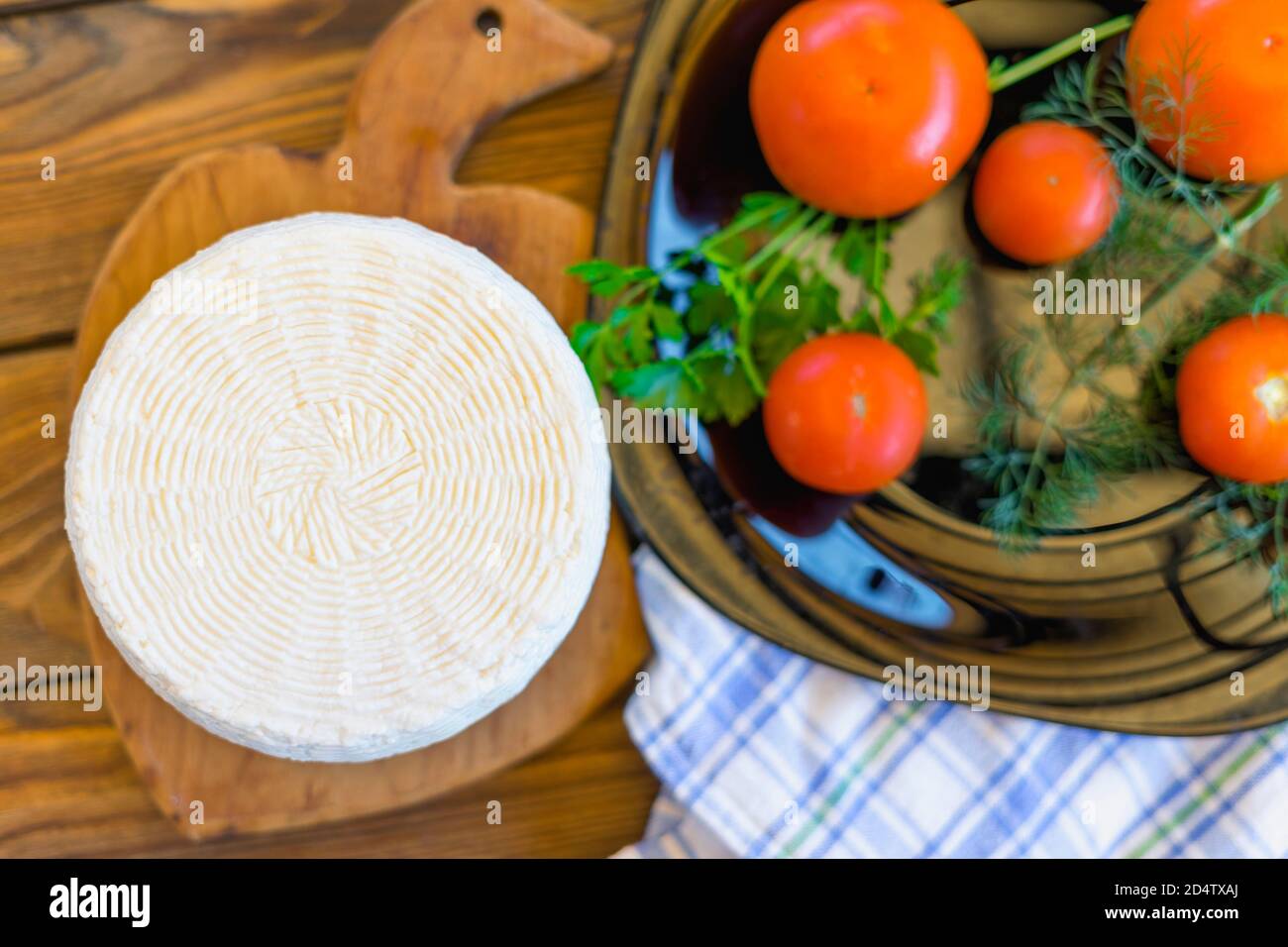 Testa di formaggio su tavola di legno su tavola di legno servita con pomodori e verdure fresche e asciugamano. Formaggio fatto in casa. Concetto di cibo. Messa a fuoco selettiva. Foto Stock