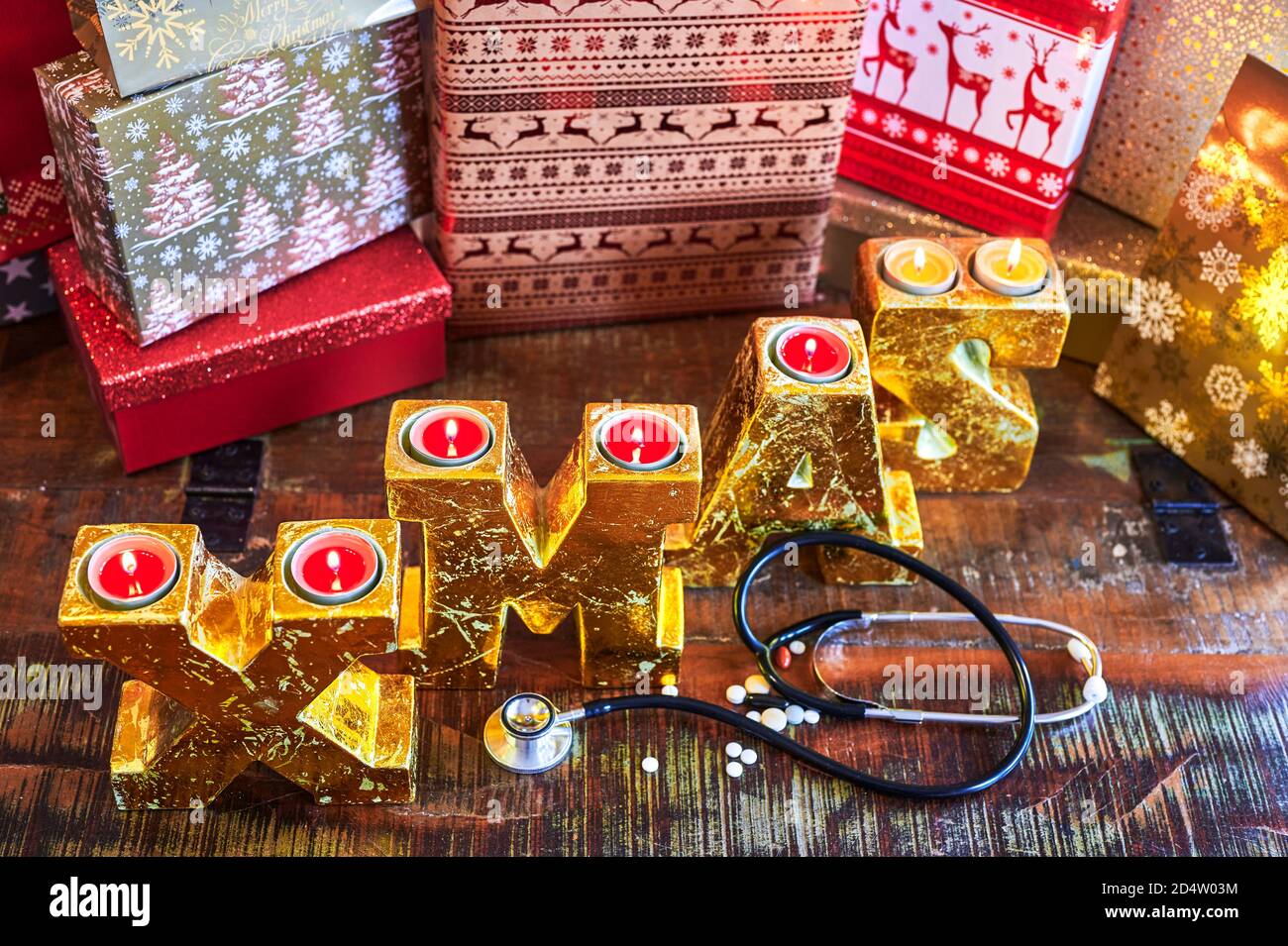 Il testo XMAS fatto di lettere d'oro su una superficie di legno combinato con pillole e uno stetoscopio. Foto Stock