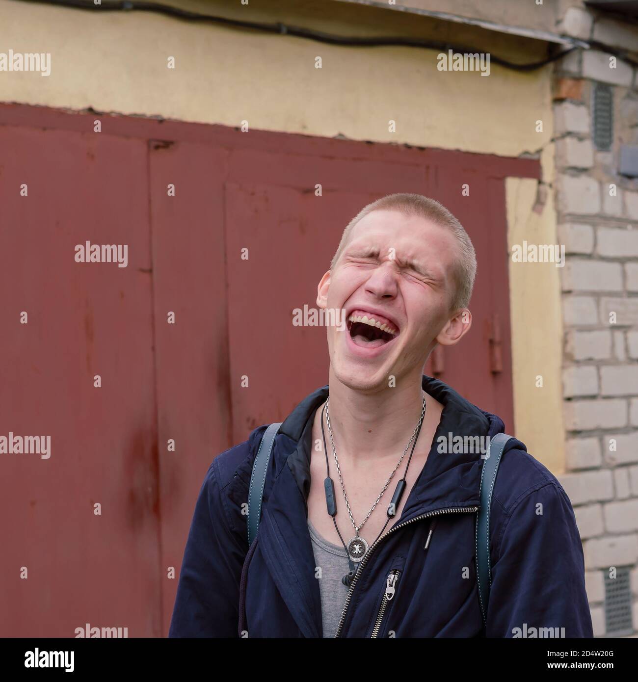 Ritratto di un giovane urlando di dolore a occhi chiusi, isterico. Un uomo con capelli corti, cuffie e un amuleto argentato intorno al collo. E umano Foto Stock