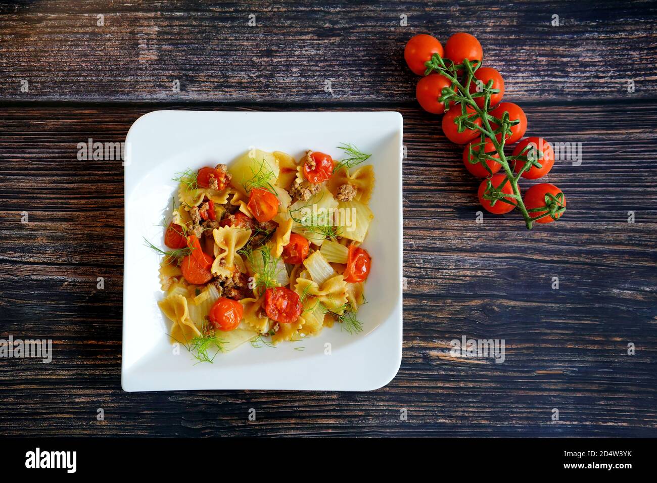 Cucina casalinga tedesca: Finocchio fresco con carne tritata, pasta e pomodori su un piatto bianco con fondo tavola in legno. Foto Stock