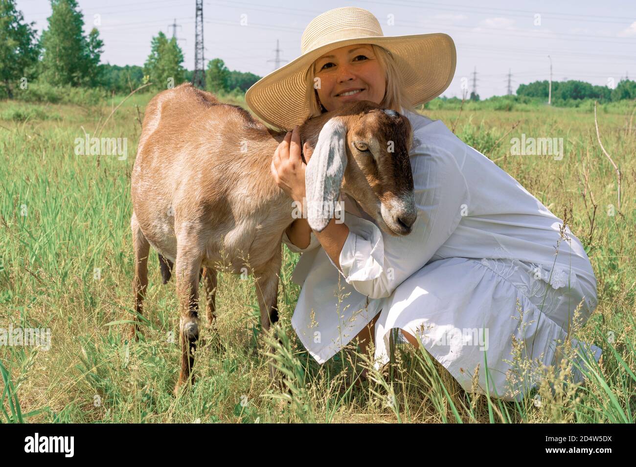 Una donna in un cappello di paglia abbraccia una capra anglo-nubiana. Un contadino con una capra nubiana. Foto Stock