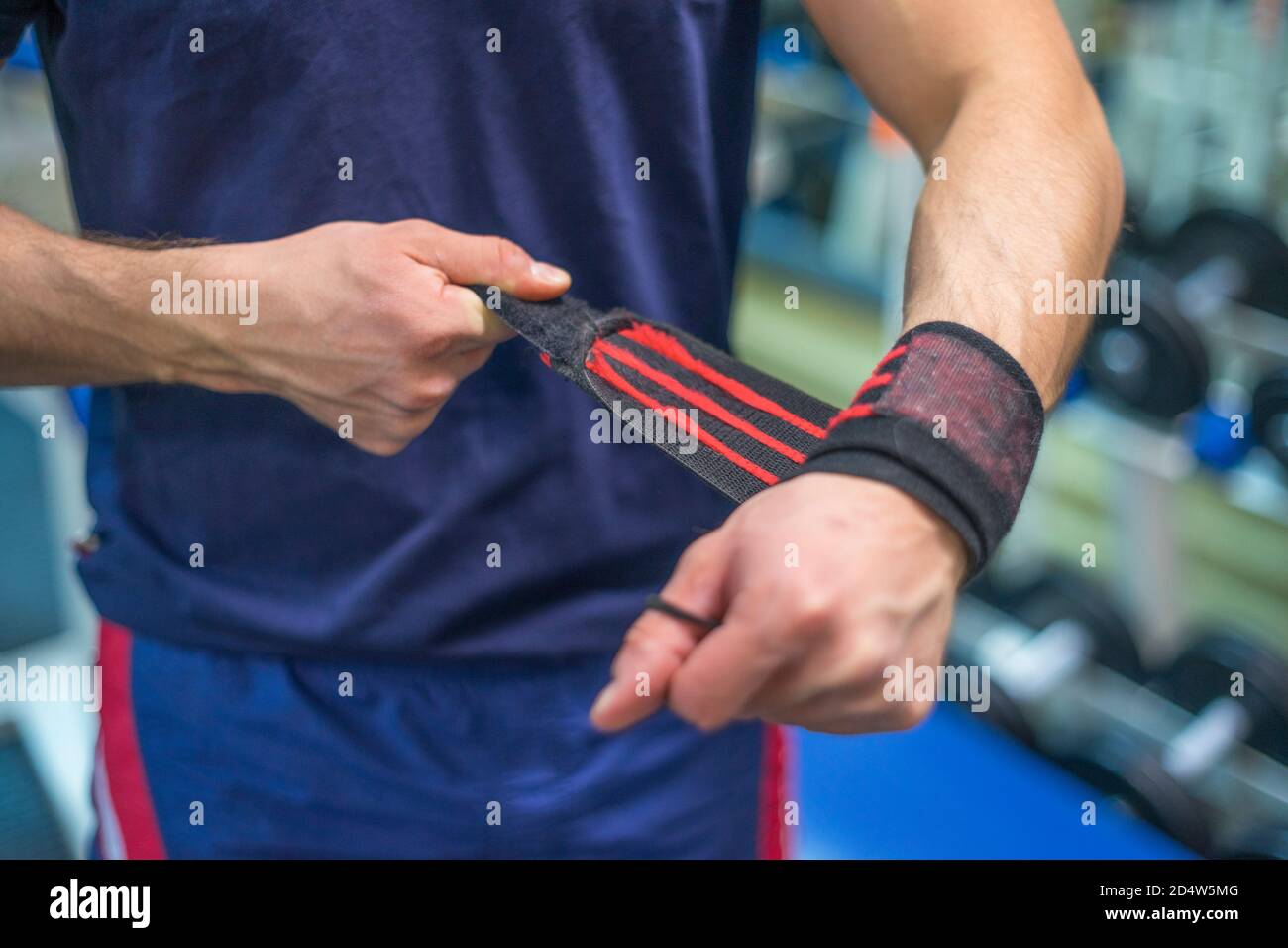 Un uomo in palestra che regola i braccialetti prima di sollevarli. Pressa da banco. Le fasce da polso si avvicinano. Foto Stock