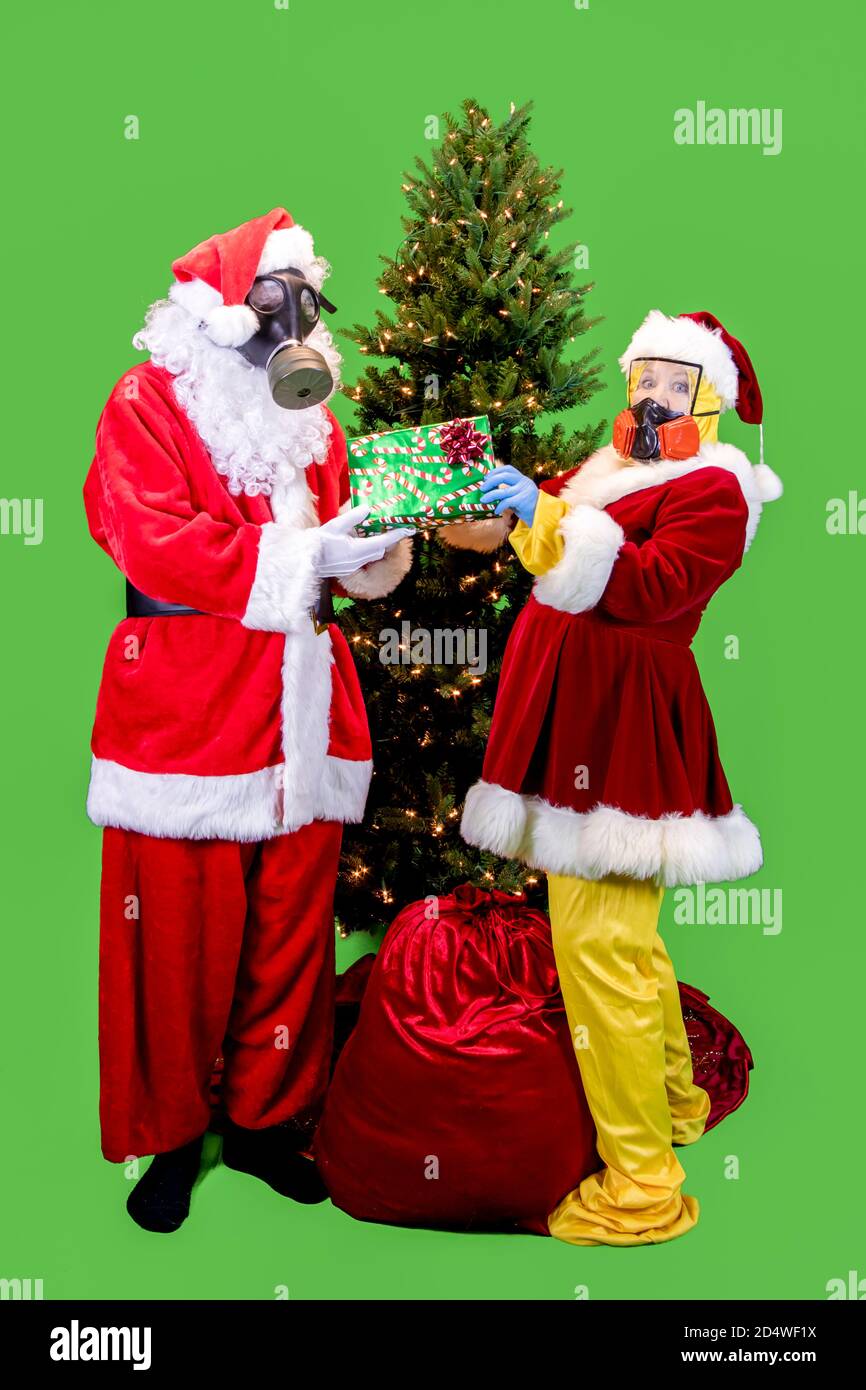Babbo Natale e la signora vestita in ppe, o indumenti protettivi personali, compresi guanti, maschere e abiti che scambiano regali sotto l'albero di Natale con rem Foto Stock