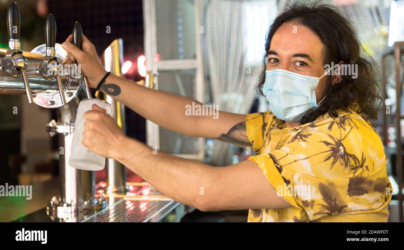 Ritratto di un barista che serve una brocca di birra al bar. Indossa una maschera facciale. Concetto di nuova normalità. Foto Stock