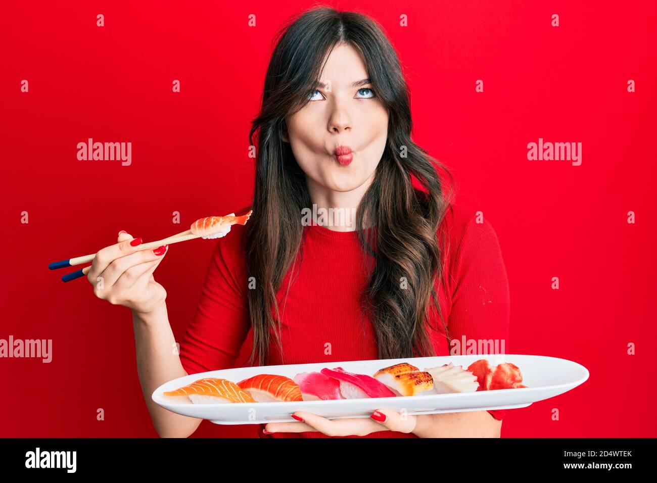 Giovane bella caucasica ragazza mangiare sushi utilizzando bastoncini di pesce faccia con la bocca e squinting occhi, pazzo e comico. Foto Stock