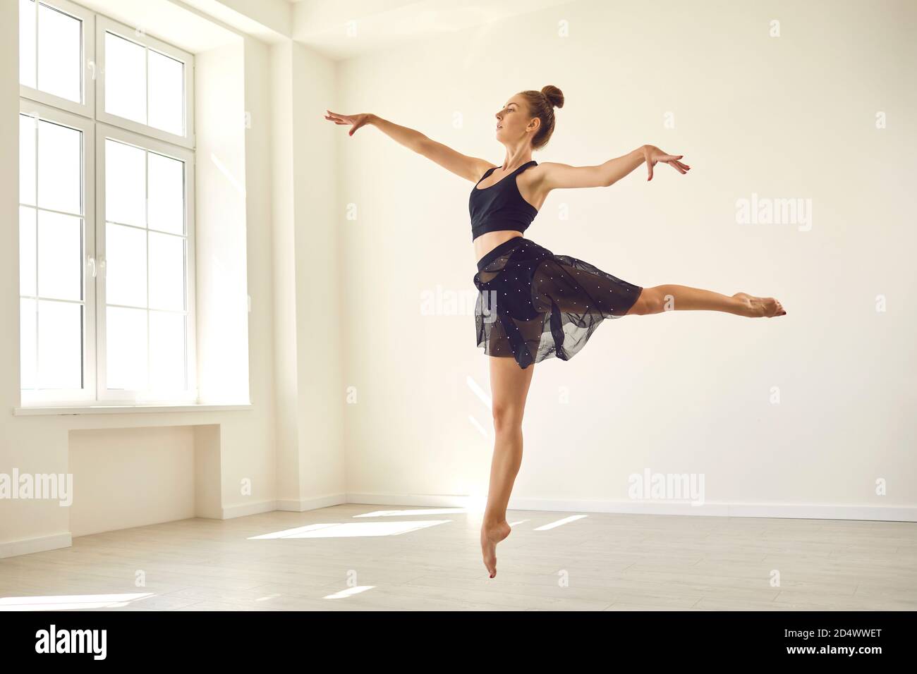 Giovane donna snella che balla in studio, pratica salti fouette, preparandosi per lo spettacolo Foto Stock