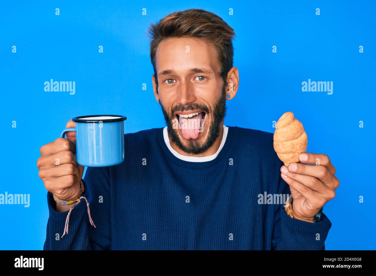 Bell'uomo caucasico con barba bevendo una tazza di caffè e croissant che si  stacca la lingua fuori felice con l'espressione divertente Foto stock -  Alamy