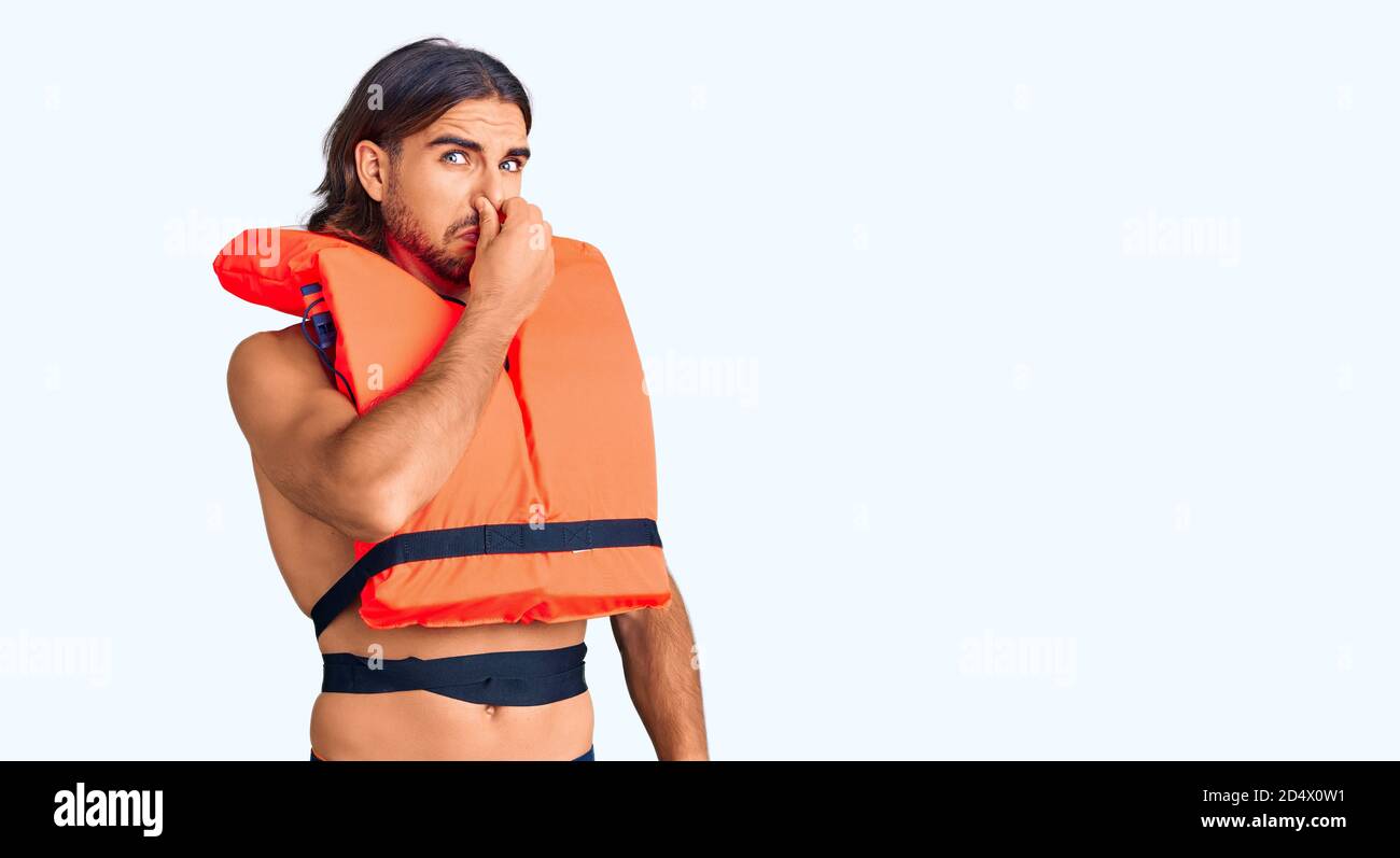 Giovane bell'uomo che indossa giubbotto di salvataggio nautico che odora qualcosa di stinoso e disgustoso, odore intollerabile, trattenendo il respiro con le dita sul naso. Male s Foto Stock