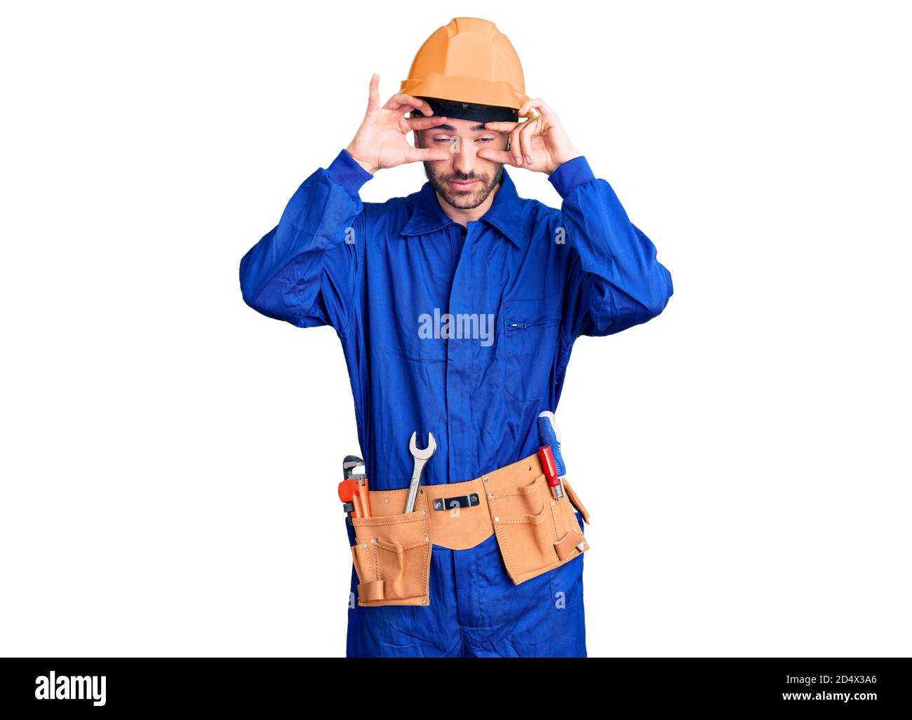 Giovane uomo ispanico che indossa uniforme operaio cercando di aprire gli occhi con le dita, sonnolento e stanco per la fatica mattutina Foto Stock
