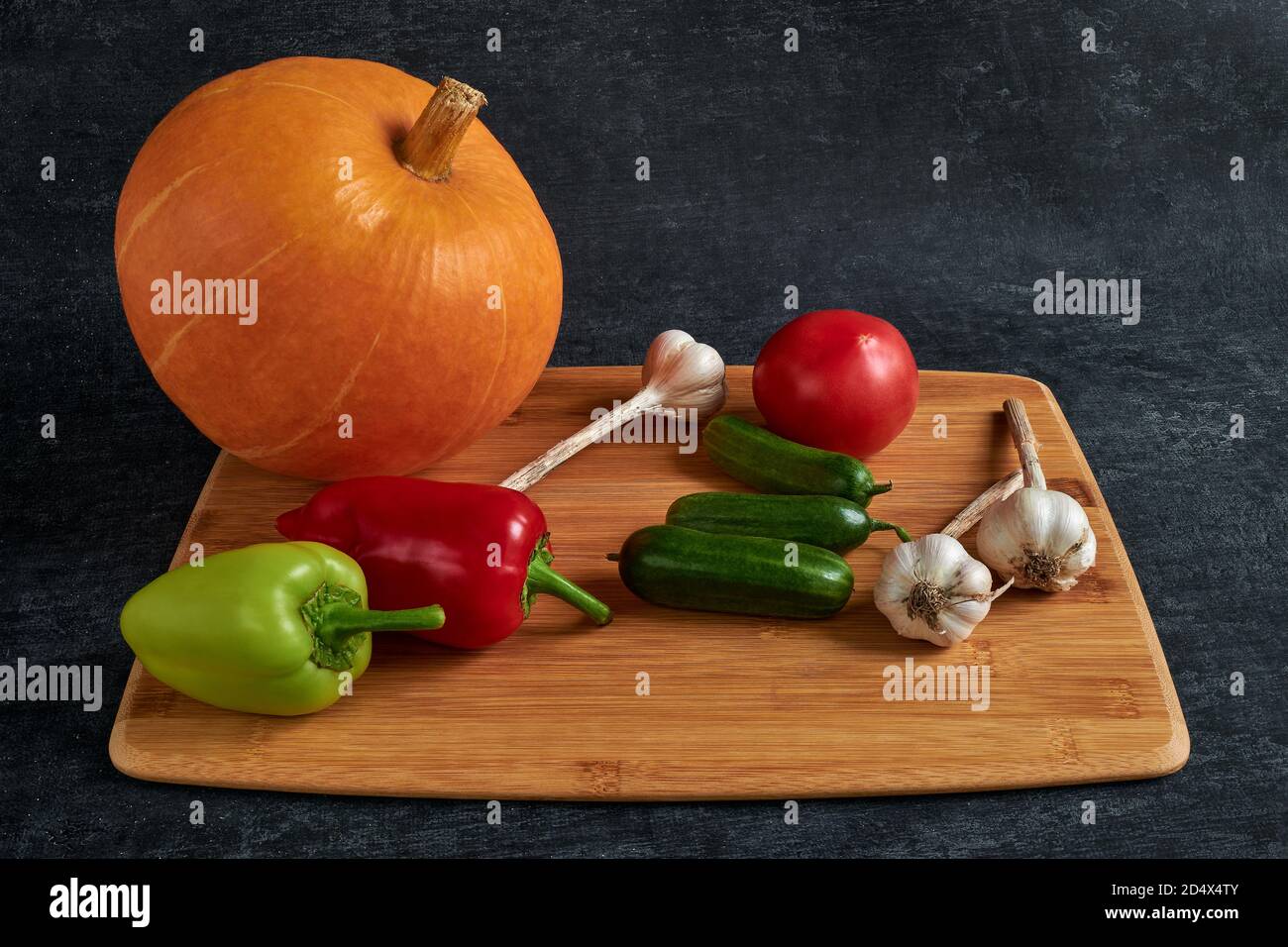 Zucca su un tagliere con pepe dolce, aglio, cetrioli e pomodori, stile scuro Foto Stock