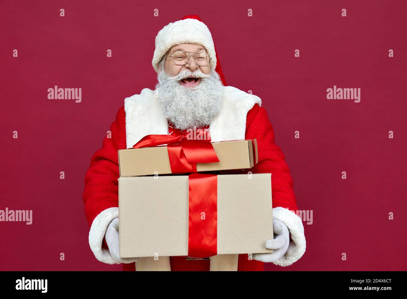 Felice Babbo Natale che tiene regali, ridendo, in piedi su sfondo rosso. Foto Stock