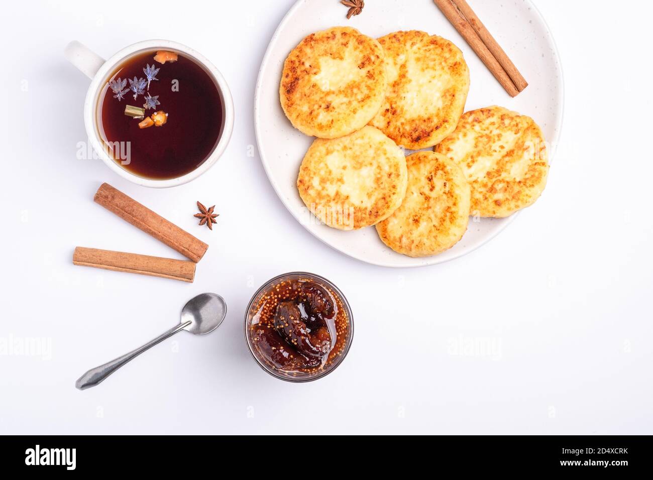 Frittelle di formaggio cottage con marmellata di fichi e tè nero aromatico caldo, umore della colazione di Natale con anice e cannella su sfondo bianco, vista dall'alto Foto Stock