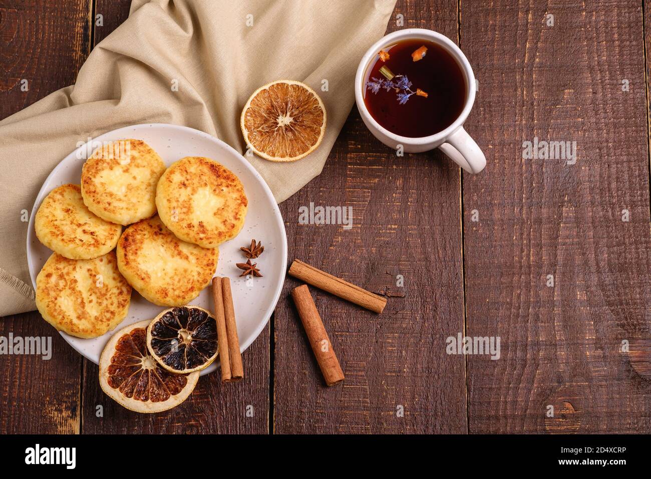 Frittelle di formaggio cottage con tè nero aromatico caldo, umore di prima colazione di Natale con anice, cannella e agrumi secchi su sfondo di legno, vista dall'alto Foto Stock