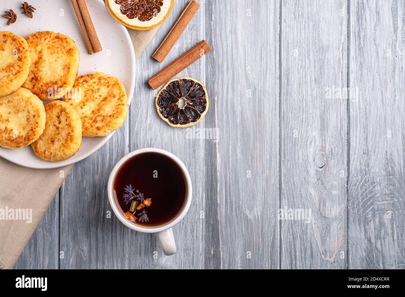 Frittelle di formaggio cottage con tè nero aromatico caldo, umore di prima colazione di Natale con anice, cannella e agrumi secchi su sfondo di legno, vista dall'alto Foto Stock