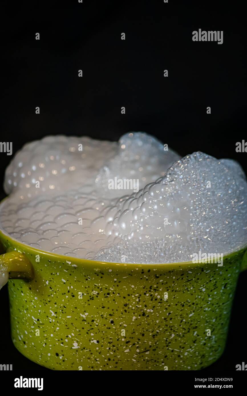 suds che cresce sulla cima di un contenitore di ceramica verde con uno sfondo nero Foto Stock