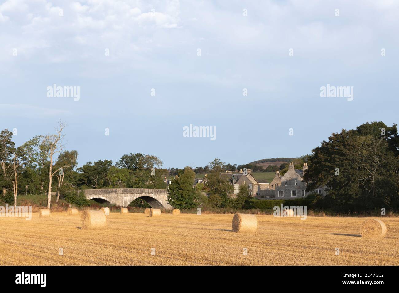 Un campo di stoppie con balle di paglia al Ponte di Alford in Aberdeenshire, guardando verso il Ponte di strada sul Fiume Don Foto Stock