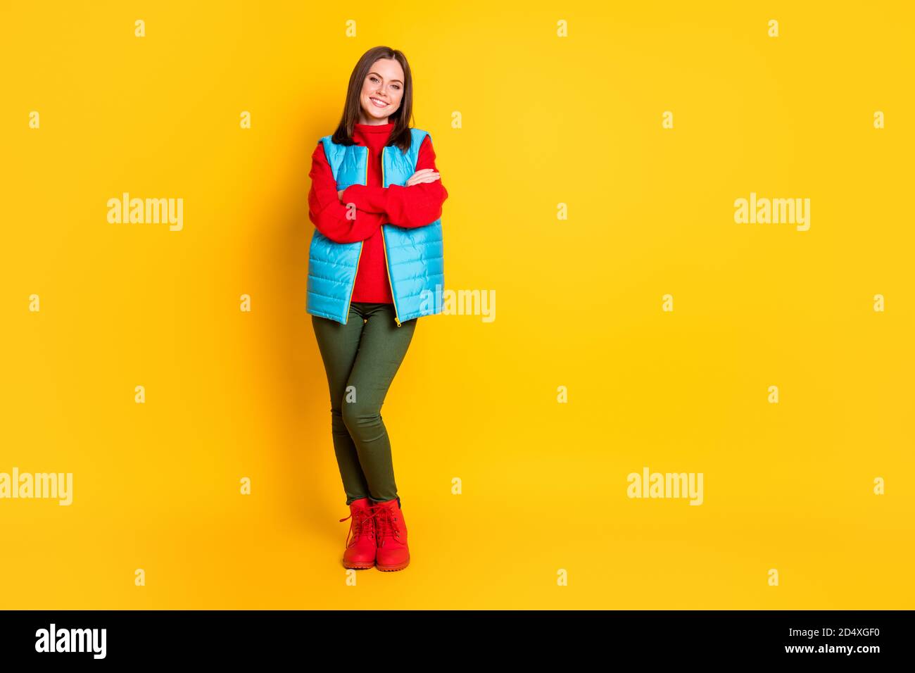 Foto a lunghezza intera di bella giovane donna sorridente ripiegata le mani si sono assicurate aspetto in attesa di sci tempo indossare pantaloni verdi blu stivali da maglione rosso gilet Foto Stock