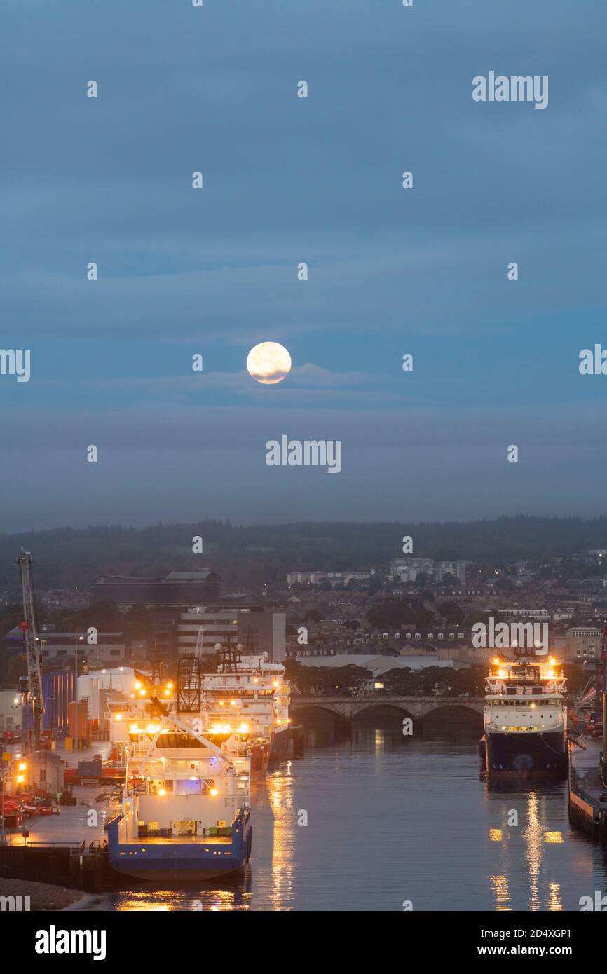 Una Luna piena sulla foce del fiume Dee ad Aberdeen, Scozia, con navi di sostegno per le piattaforme petrolifere del Mare del Nord ormeggiate lungo i moli Foto Stock