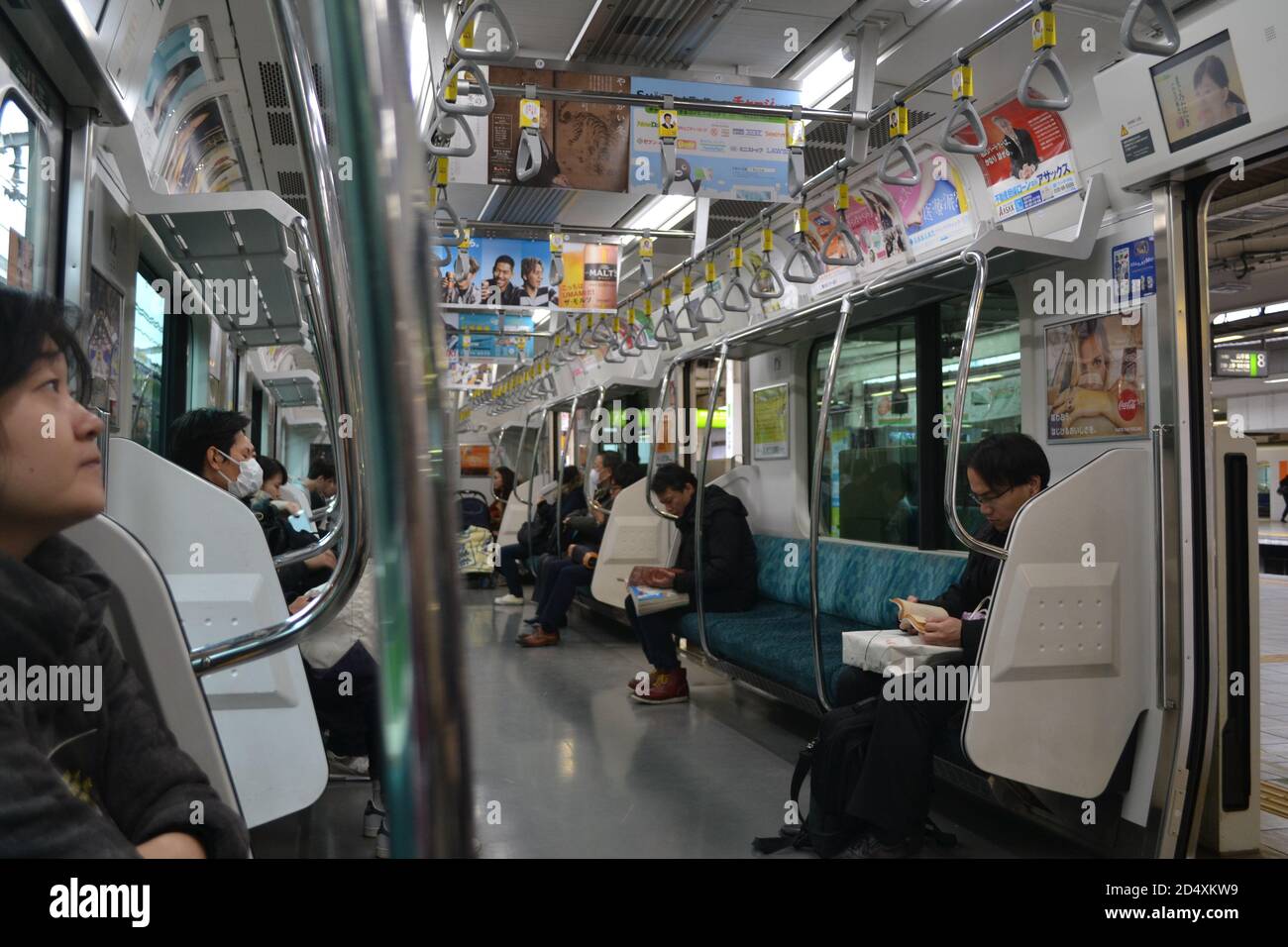 Tokyo, Japan-02/23/16: All'interno di un treno locale che attraversa Tokyo: Un gruppo diversificato di persone che si siedono sui loro posti in treno e svolgono varie attività. Foto Stock