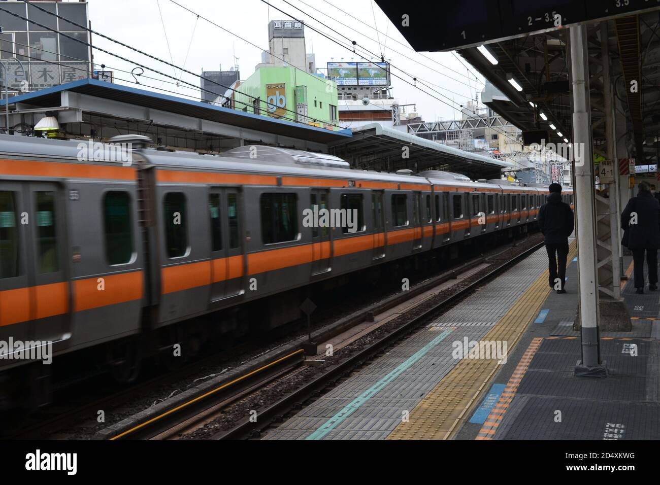 Tokyo, Japan-02/23/16: Persone che camminano lungo la piattaforma ferroviaria mentre il treno locale viaggia lungo la linea ferroviaria ad una grande velocità. Foto Stock