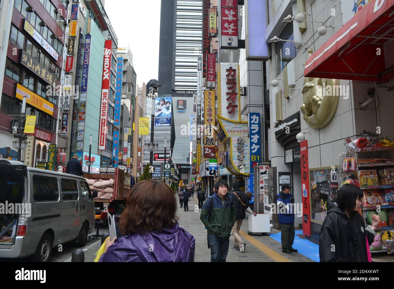 Tokyo, Japan-2/24/16: Lungo le strade trafficate del quartiere di Shinjuku; una statua a grandezza naturale di Godzilla si erge sugli edifici con tonnellate di cartelli per negozi. Foto Stock