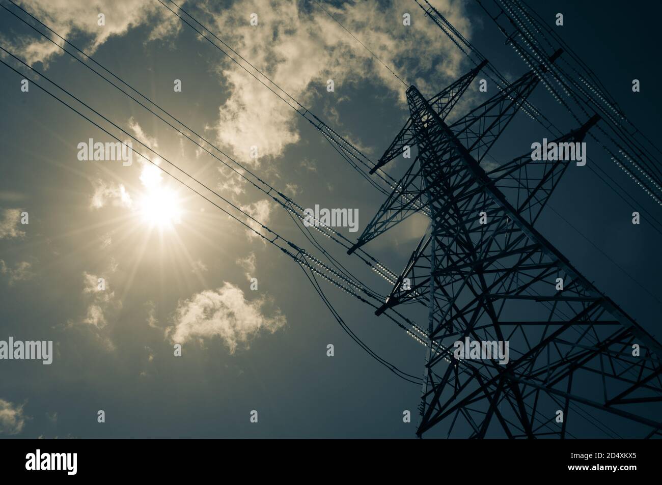 Un pilone elettrico si erge alto nel caldo sole estivo con alcune nuvole wisy. Concetto di energia solare. Foto Stock
