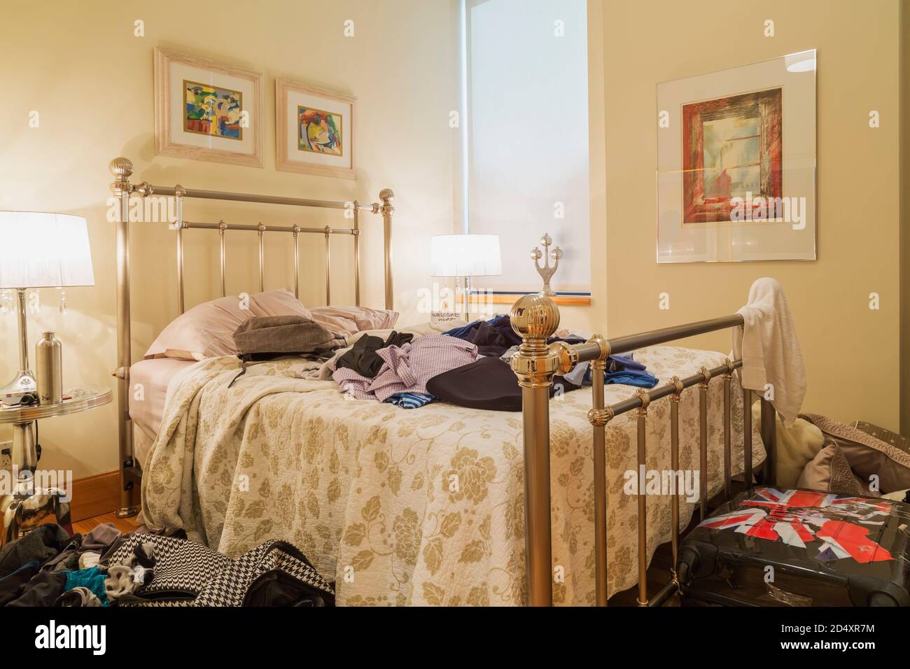 Vestiti sulla parte superiore del letto di misura regina e sul pavimento nella camera da letto disordinata dell'adolescente all'interno di un condominio di lusso. Foto Stock