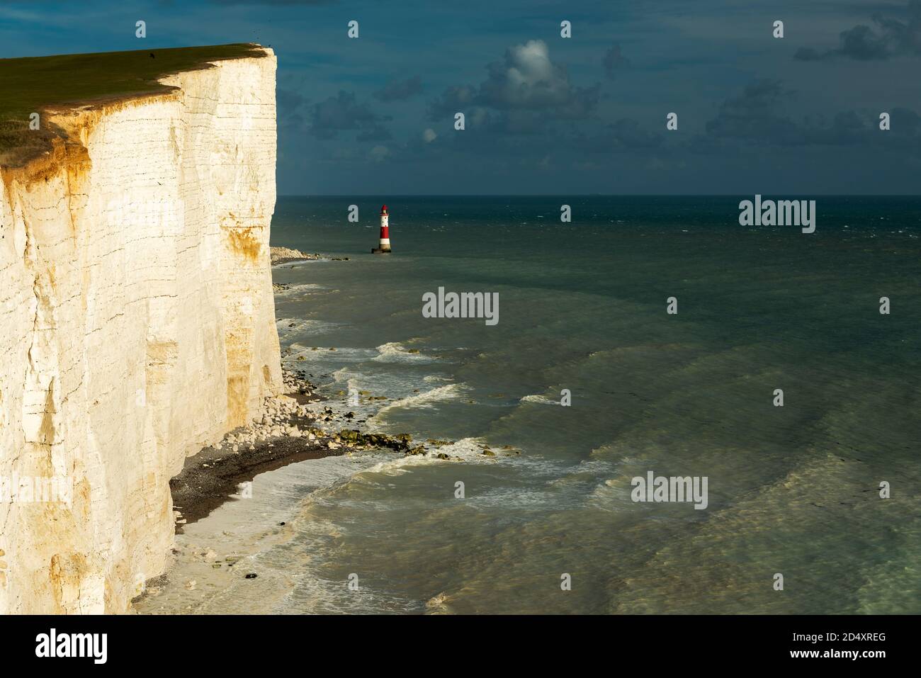 Il sole oscura tra le nuvole scure che si avvicinano da ovest per illuminare il faro e le scogliere a Beachy Head in un pomeriggio di autunno ardente, Foto Stock