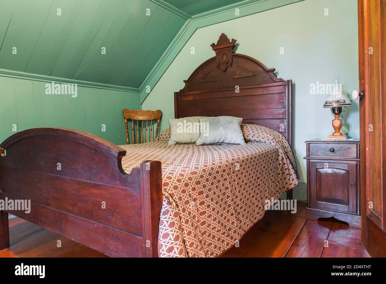 Antico letto matrimoniale con testiera in legno e pedana, comodino e sedia a dondolo con schienale in camera al piano superiore all'interno della vecchia casa. Foto Stock