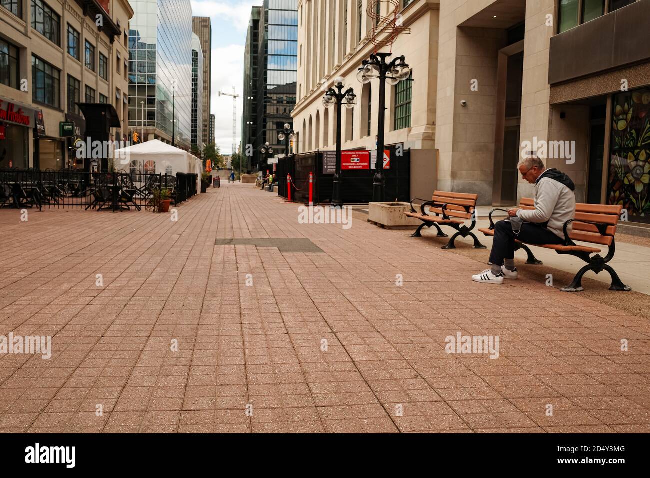 Ottawa, Ontario, Canada - 8 ottobre 2020: Un uomo usa uno smartphone su una panchina, una delle poche persone nel centro commerciale Sparks Street. La piazza esterna ha visto Foto Stock