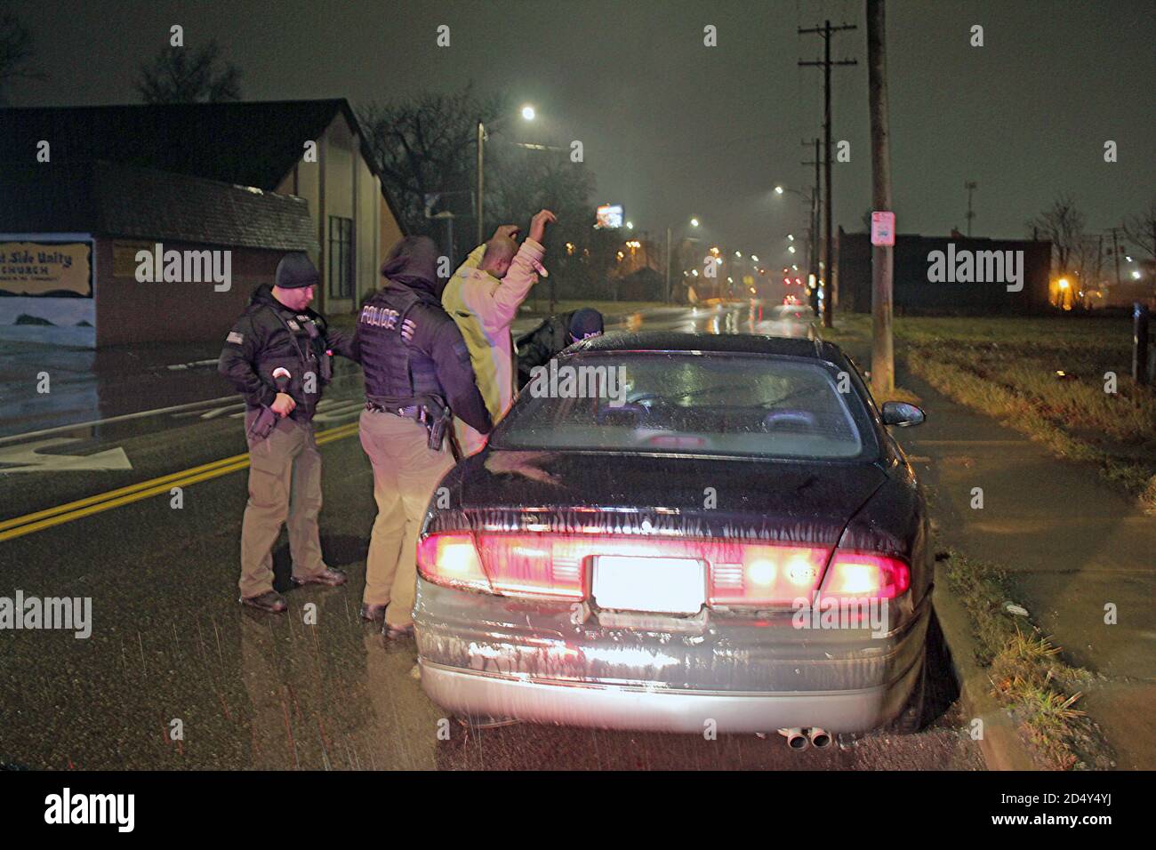 Gli agenti di polizia di Detroit detengono un uomo e cercano il suo veicolo di notte, Detroit, Michigan, USA Foto Stock