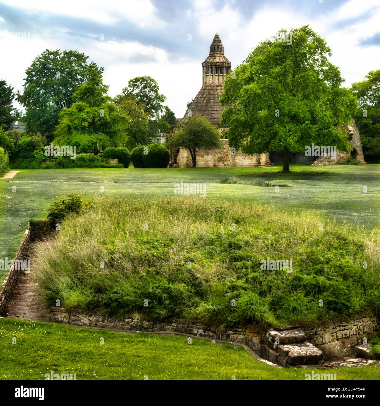 La cucina di Glastonbury Abbot Abbey con le rovine e i bagni dei monaci (necessarium) in primo piano. Giornata estiva con cielo blu e nuvole bianche. Foto Stock